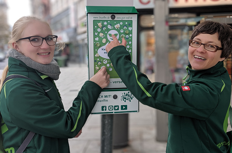 Foto: Zwei Personen nutzen eine cleanffm-Gum-Wall zur Entsorgung von Kaugummis.