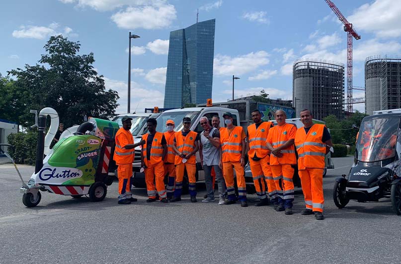 Foto: cleanffm-Express mit Stadtsauger Glutton und dem Bahnbabo vor Frankfurter Skyline.