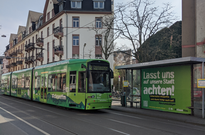 Foto: Straßenbahn und Haltestelle mit cleanffm-Kampagne ‚Lasst uns‘ im Stadtbild.