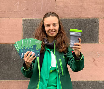Foto: Sauberkeitsbotschafterin hält mehrere Notizbücher und einen Mehrwegbecher